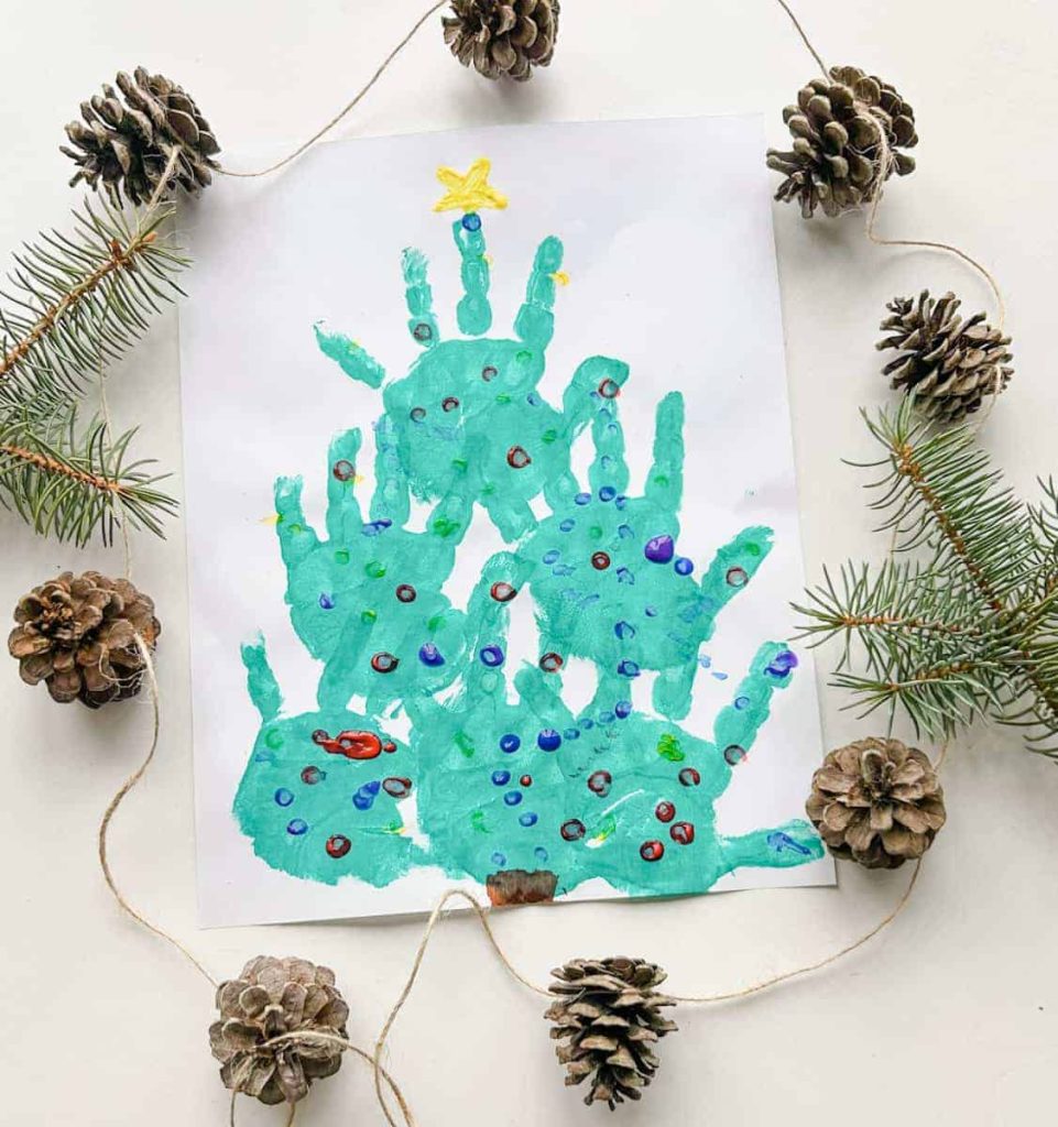 completed christmas tree handprint craft on table with pinecones around it