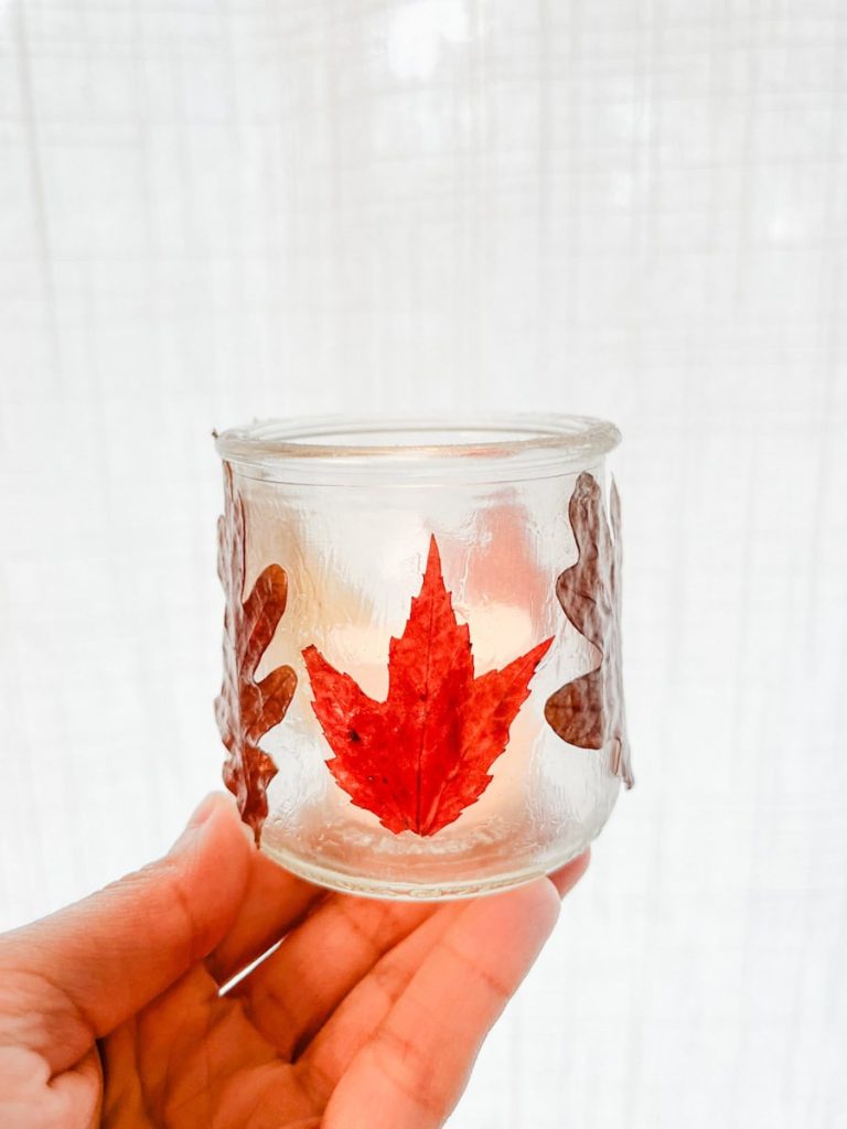 a hand holding a finished fall leaf luminary in front of a white curtain