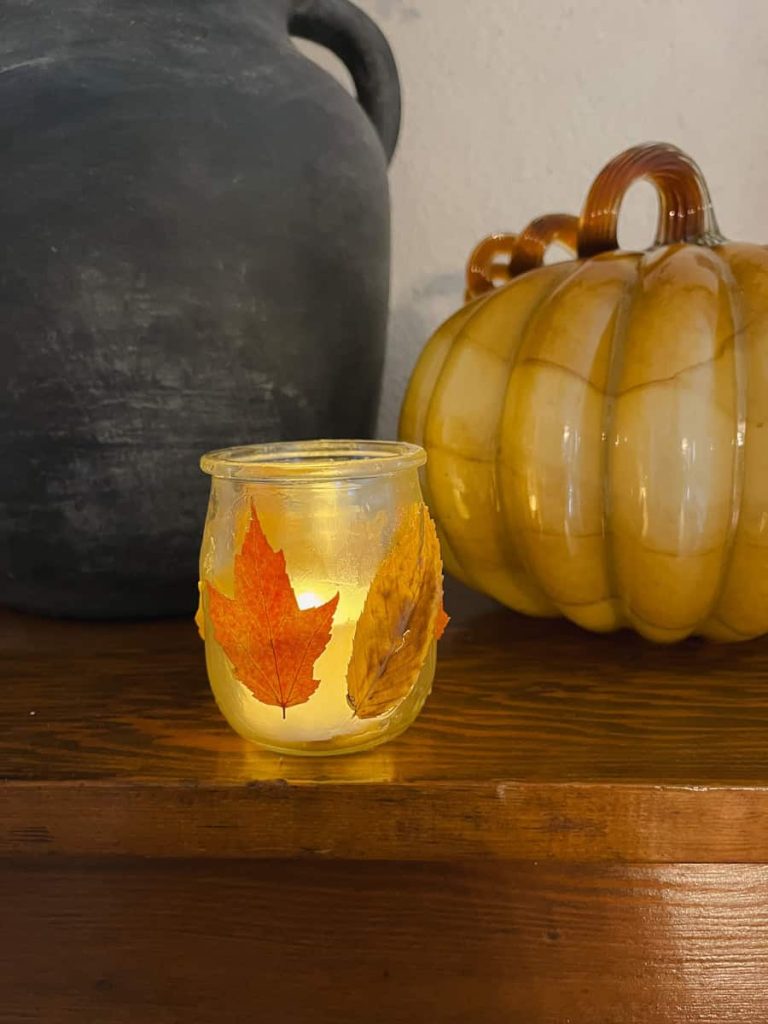 a fall leaf lantern sitting next to a glass pumpkin in the dark