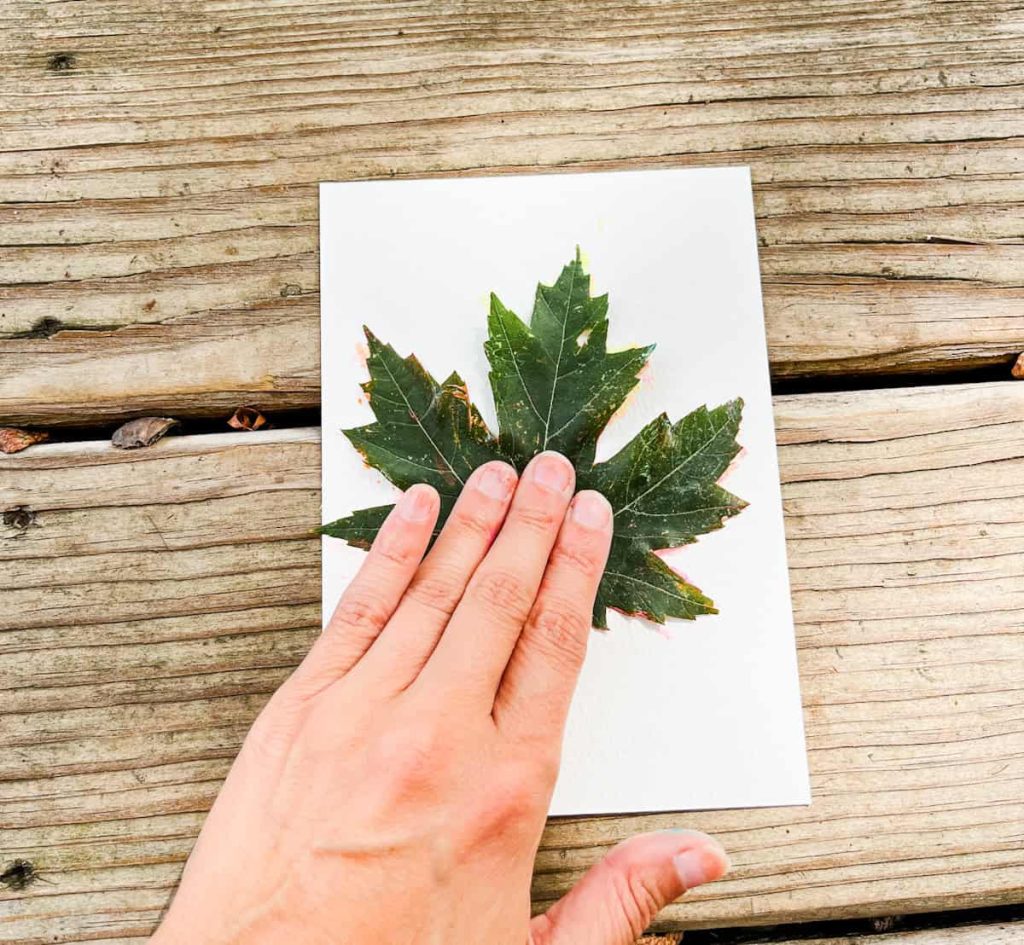 hand pressing down a painted leaf onto cardstock