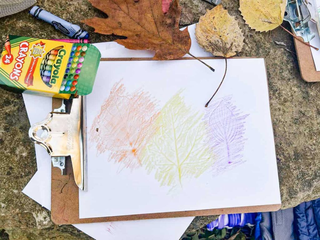 leaf rubbings on a clipboard outside next to crayons and leaves