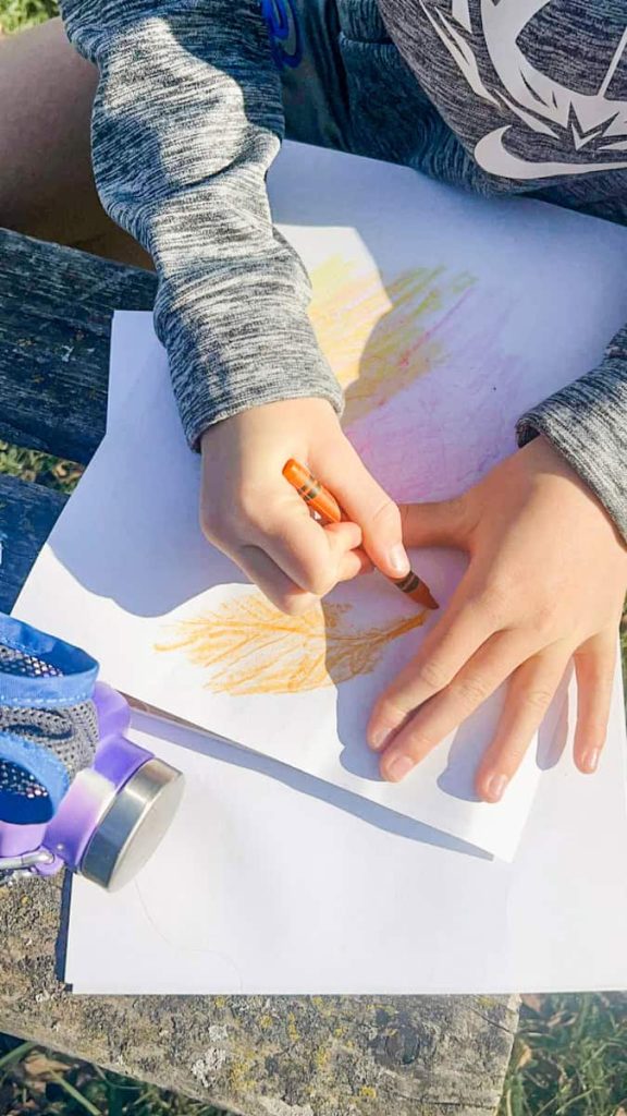 child using orange crayon to do leaf rubbing craft