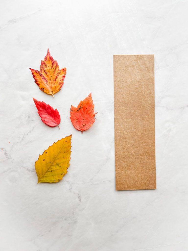 brown cardstock the shape of a bookmark sitting on counter next to small fall leaves