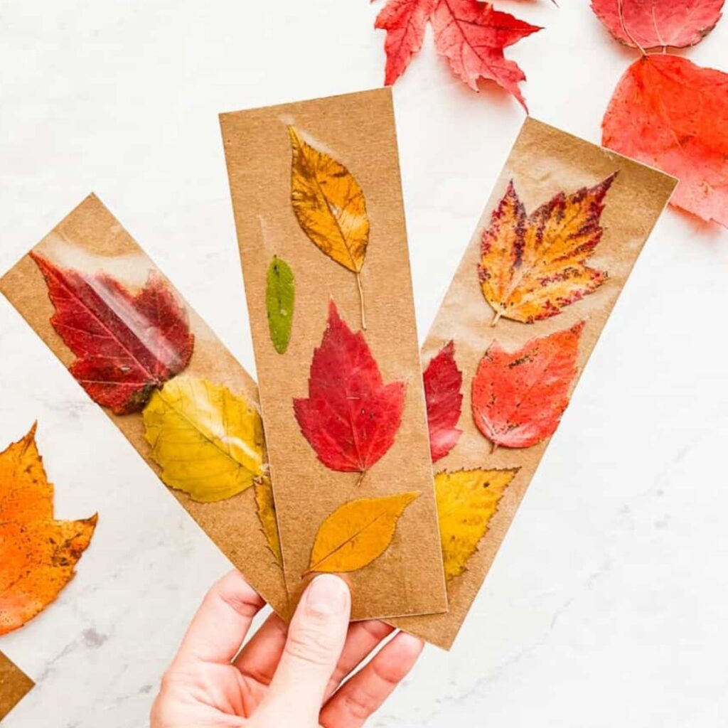 3 fall leaf bookmarks held up in front of white counter with leaves and scissors on it
