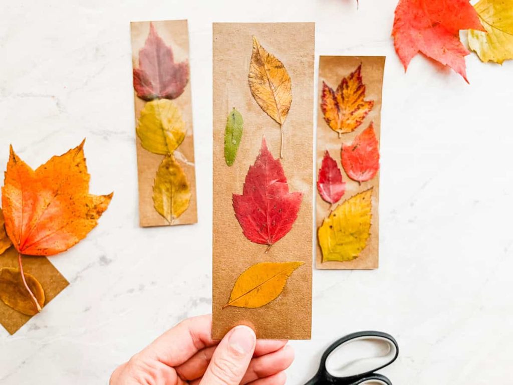 hand holding fall leaf bookmark with other bookmarks on the counter in the background