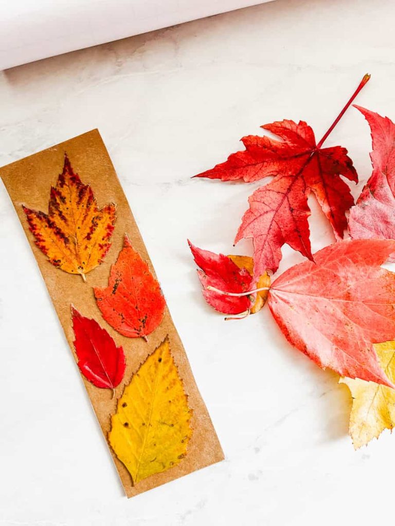 diy leaf bookmark sitting next to a colorful pile of fall leaves 