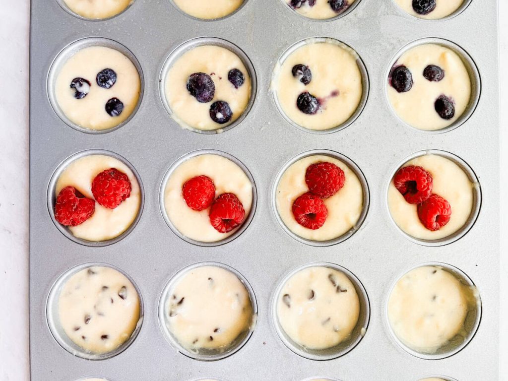 mini muffin tin filled with pancake batter with blueberries and raspberries on top
