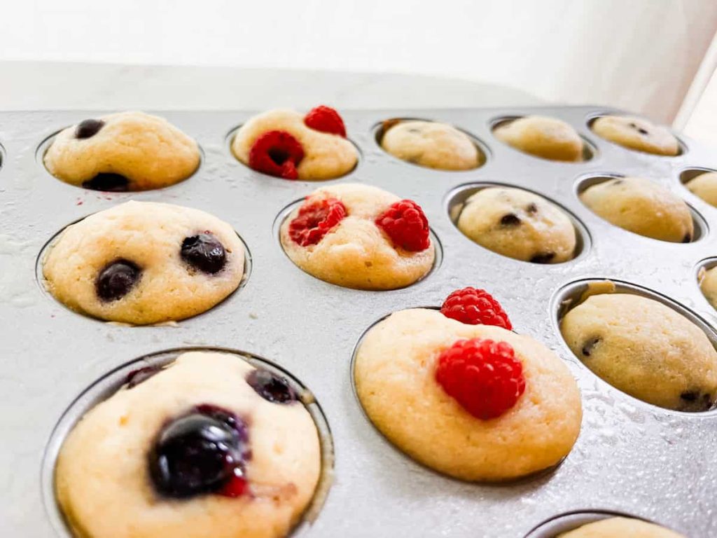 mini muffin tin filled with mini pancakes topped with raspberries and blueberries cooling in the pan
