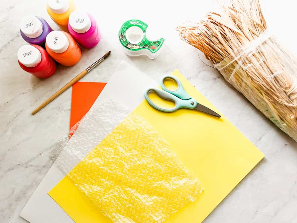 paint, tape, paintbrush, construction paper, raffia, scissors and bubble wrap sitting on the counter