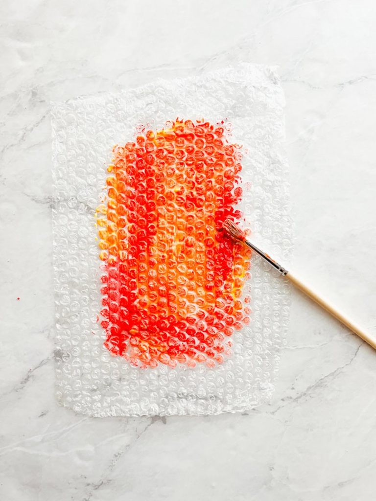red and orange painted bubble wrap on counter next to a paint brush