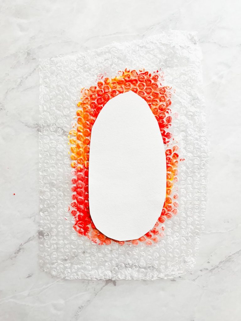 construction paper in the shape of a corn cob laid flat on top of painted bubble wrap 