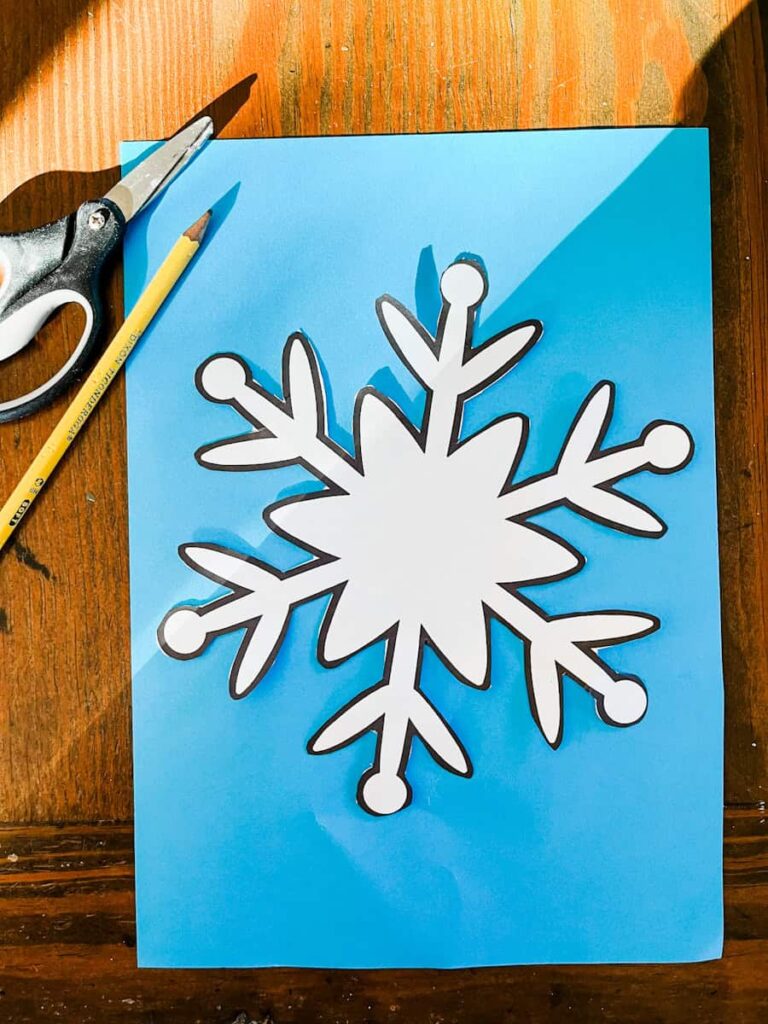 snowflake template on blue construction paper with pencil and scissors
