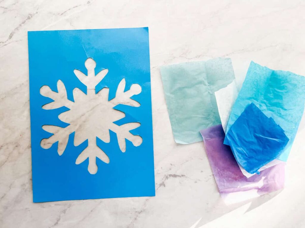 cut out snowflake outline and tissue paper sitting on counter