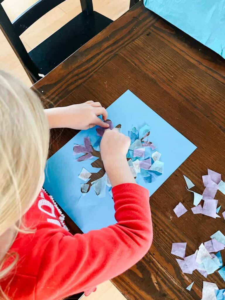 child placing tissue paper on the suncatcher template
