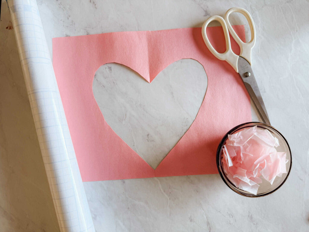 construction paper with heart outline cut out with scissors and tissue paper next to it
