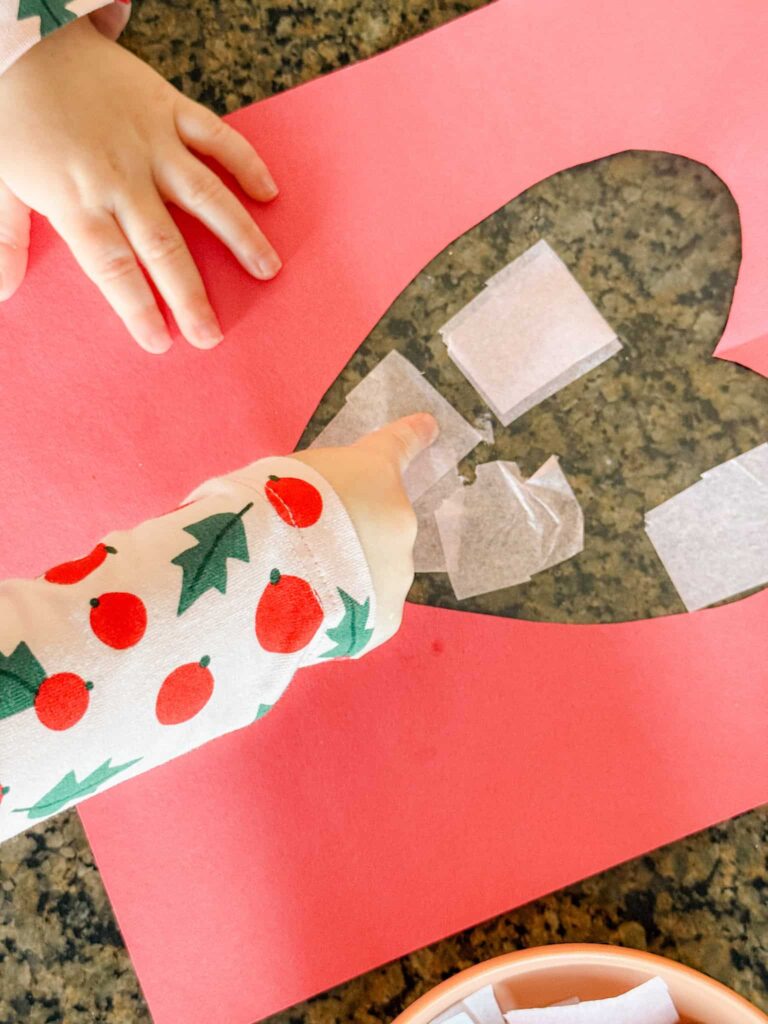 child placing tissue paper onto contact paper