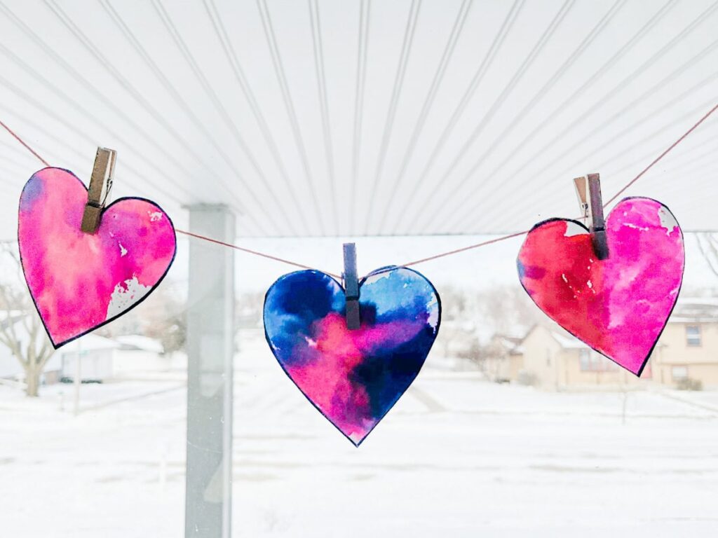 three watercolor hearts strung up in front of window