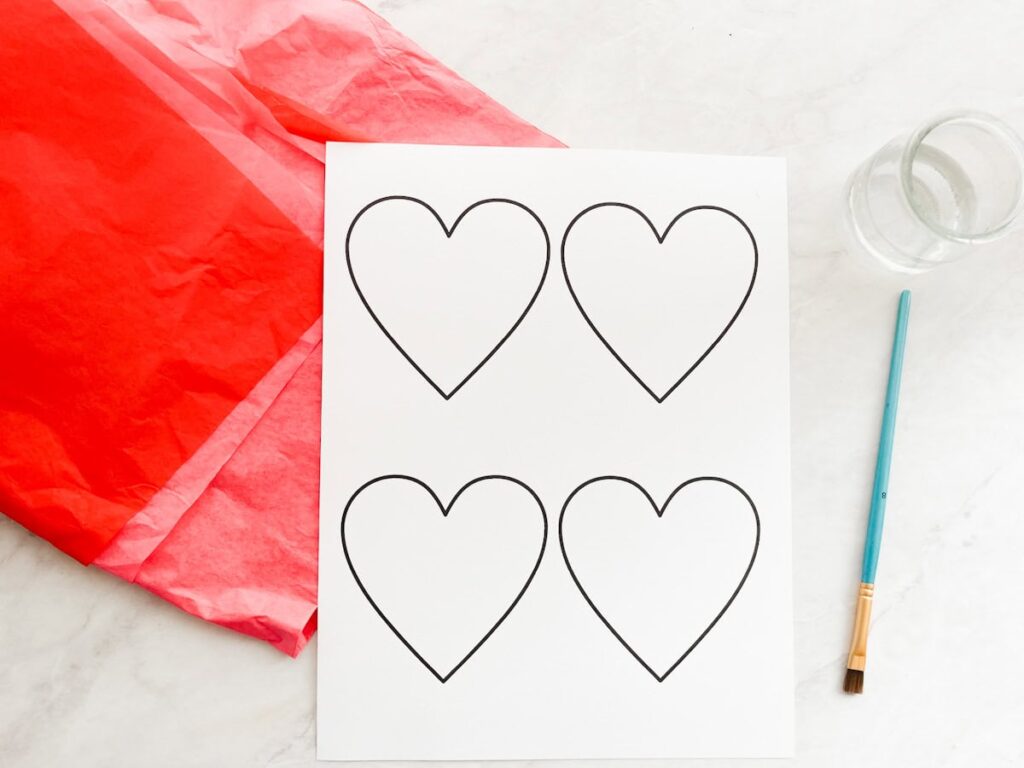 heart template, water, paint brush, tissue paper sitting on the counter