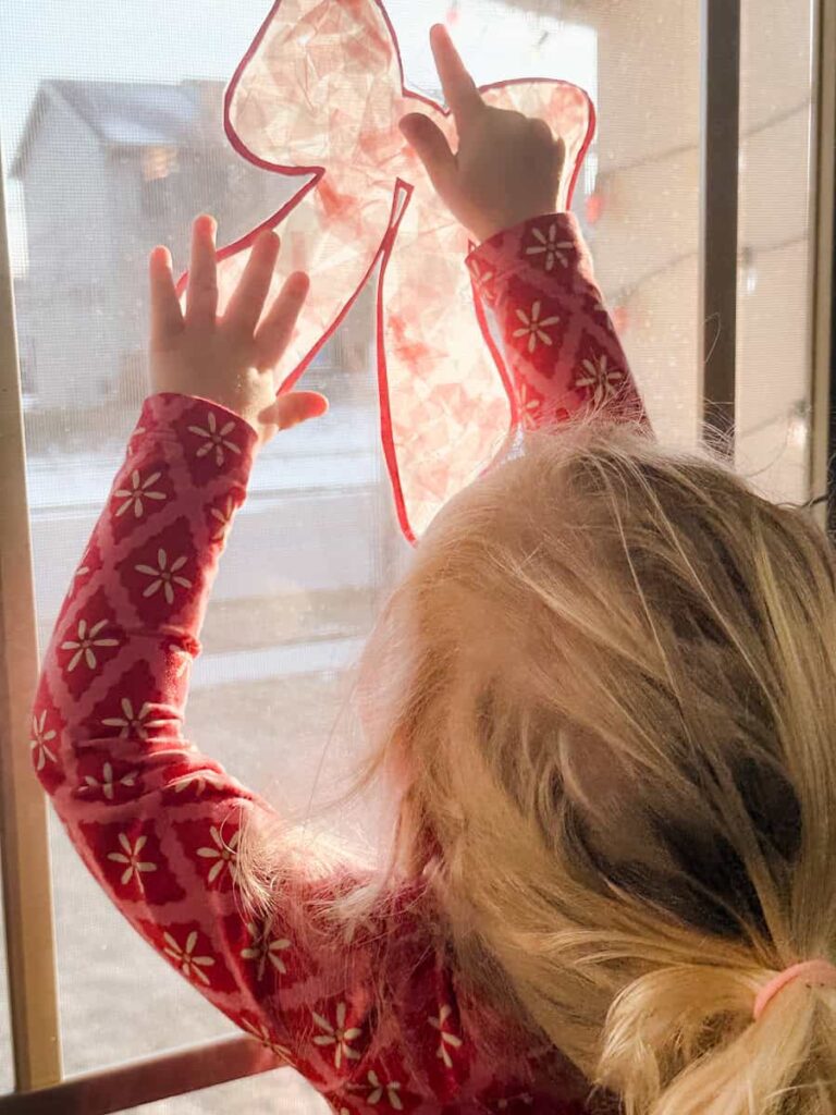child putting the completed bow suncatcher on window