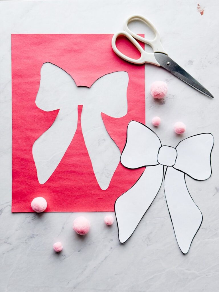 bow cut out of the construction paper with template next to it and scissors on table