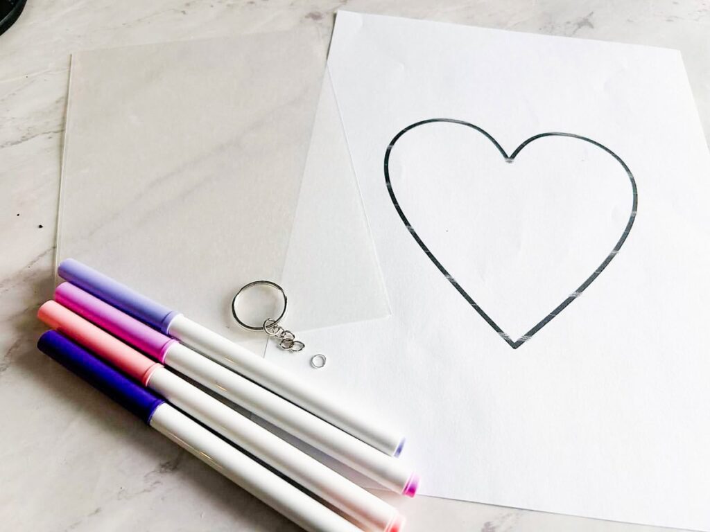 heart template, shrinky dink paper, keychain and jump ring and markers laying on table