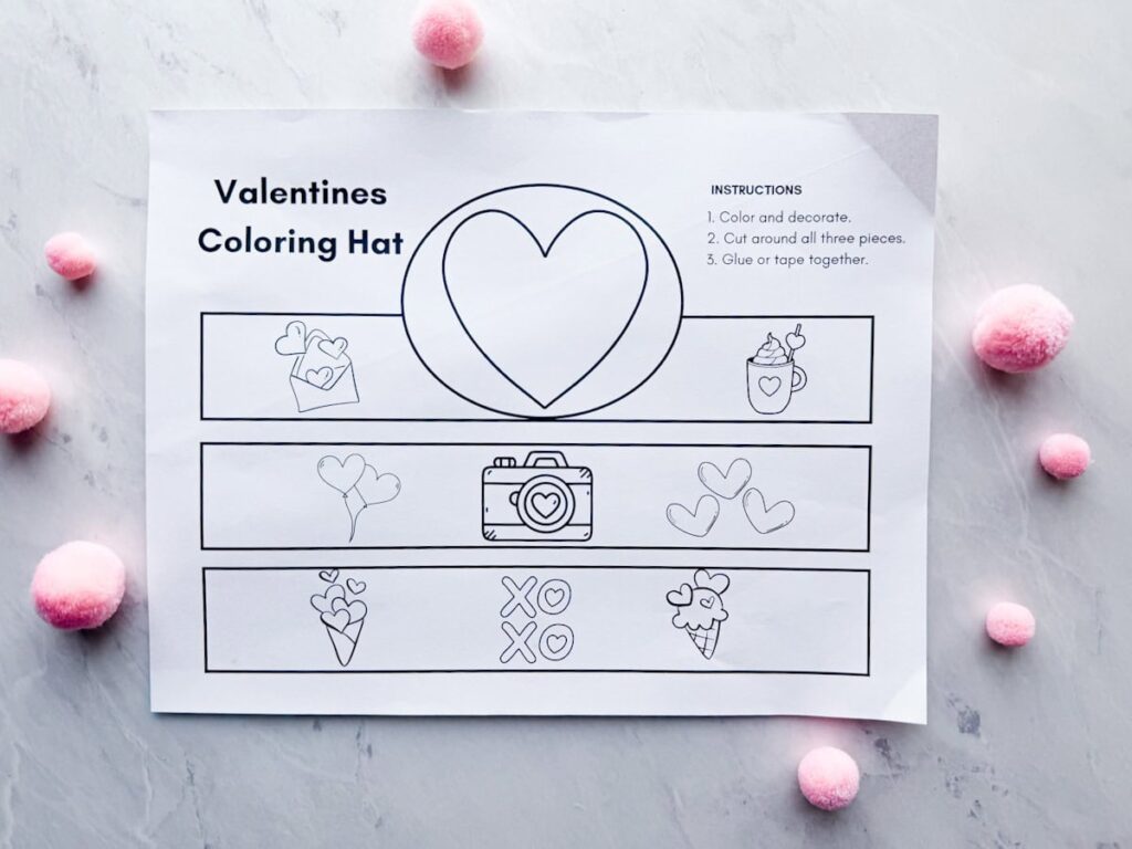 plain Valentines coloring hat on table with pink pom poms around it