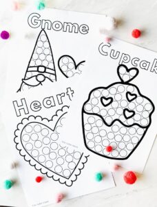 3 of the printable dot marker pages on a table with pom poms around them
