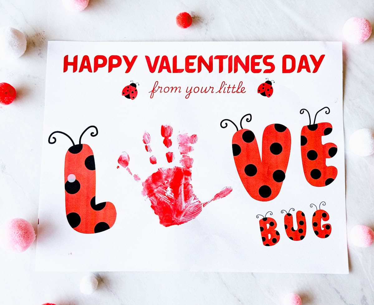 Completed printable love bug craft with handprint as the "o" and on table with pom poms around it