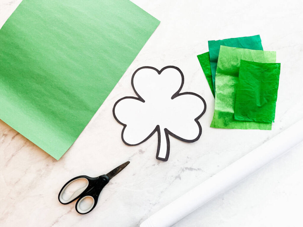 shamrock template, tissue paper, construction paper , contact paper and scissors sitting on a counter