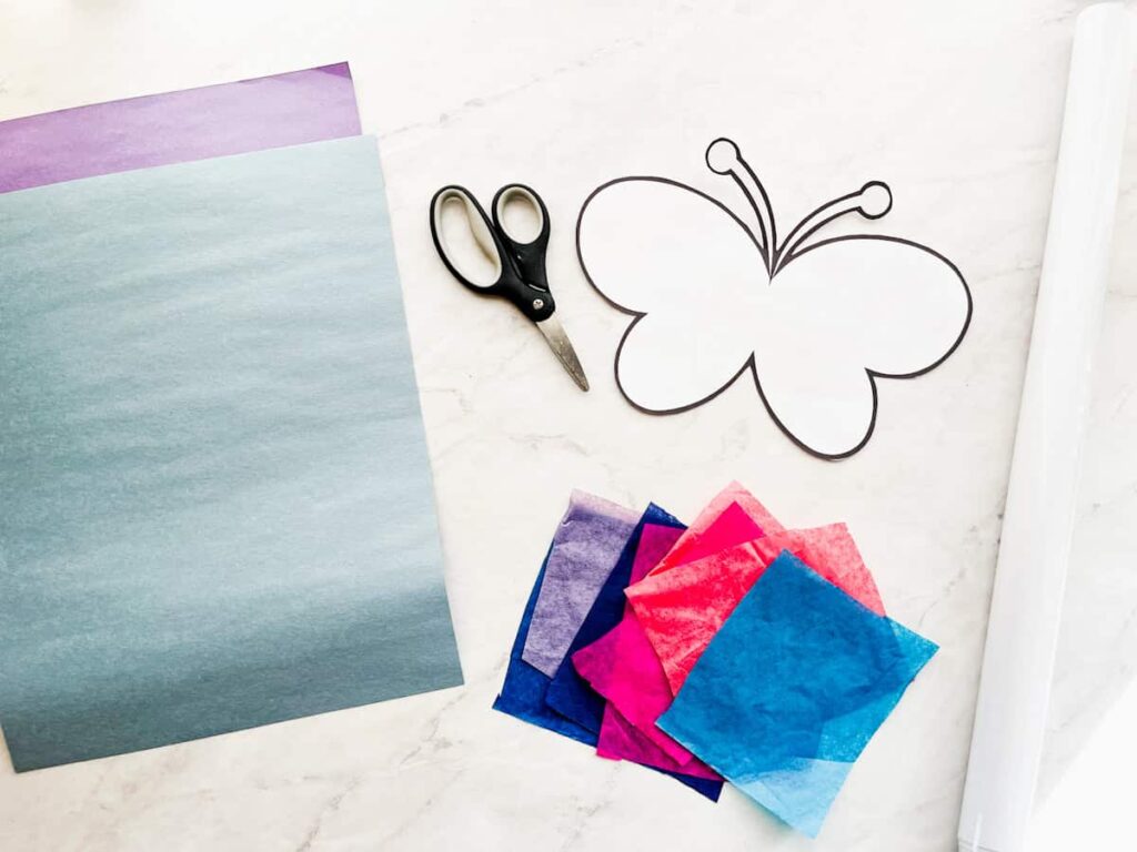 construction paper, scissors, butterfly template, tissue paper squares and contact paper sitting on a white countertop.