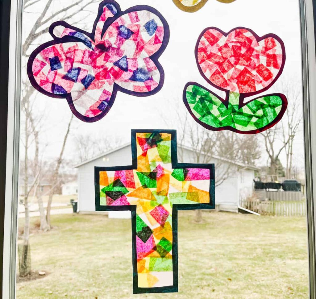 finished cross suncatcher next to tulip suncatcher and butterfly suncatcher on a window