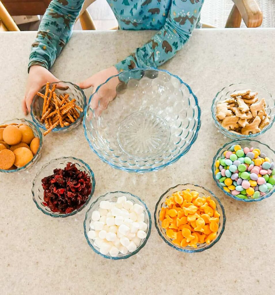 child picking up the pretzel bowl to pour in to make the snack mix