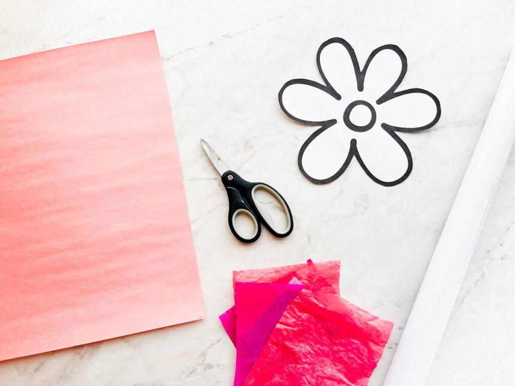 construction paper, scissors, flower template, tissue paper and contact paper sitting on a counter