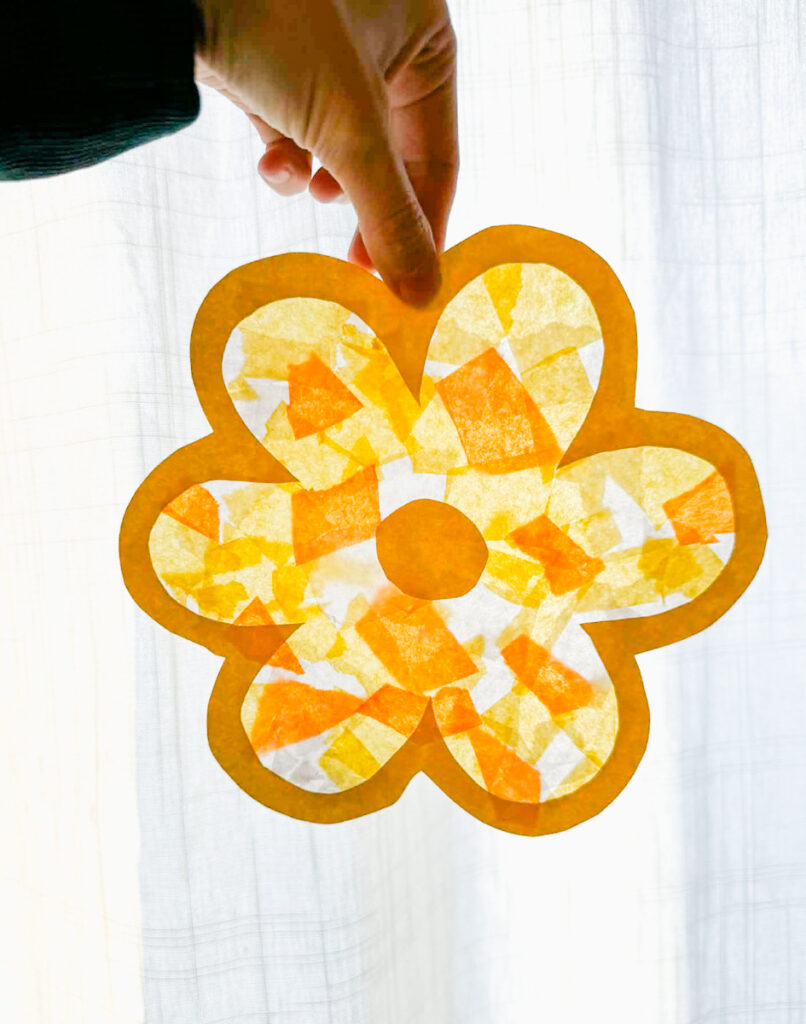 hand holding up a yellow finished flower suncatcher in front of the window