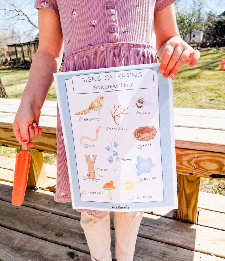 child holding signs of spring scavenger hunt and a popsicle in backyard