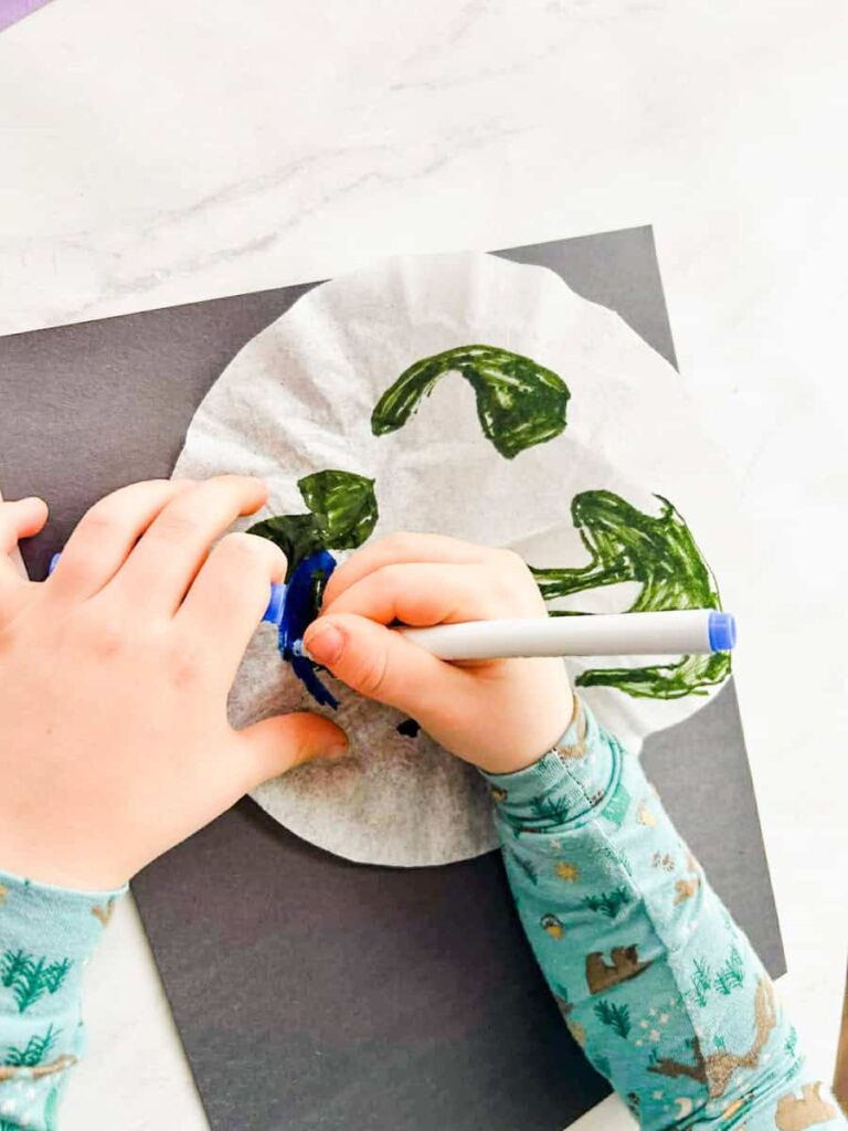 child drawing the continents on the coffee filter with green marker