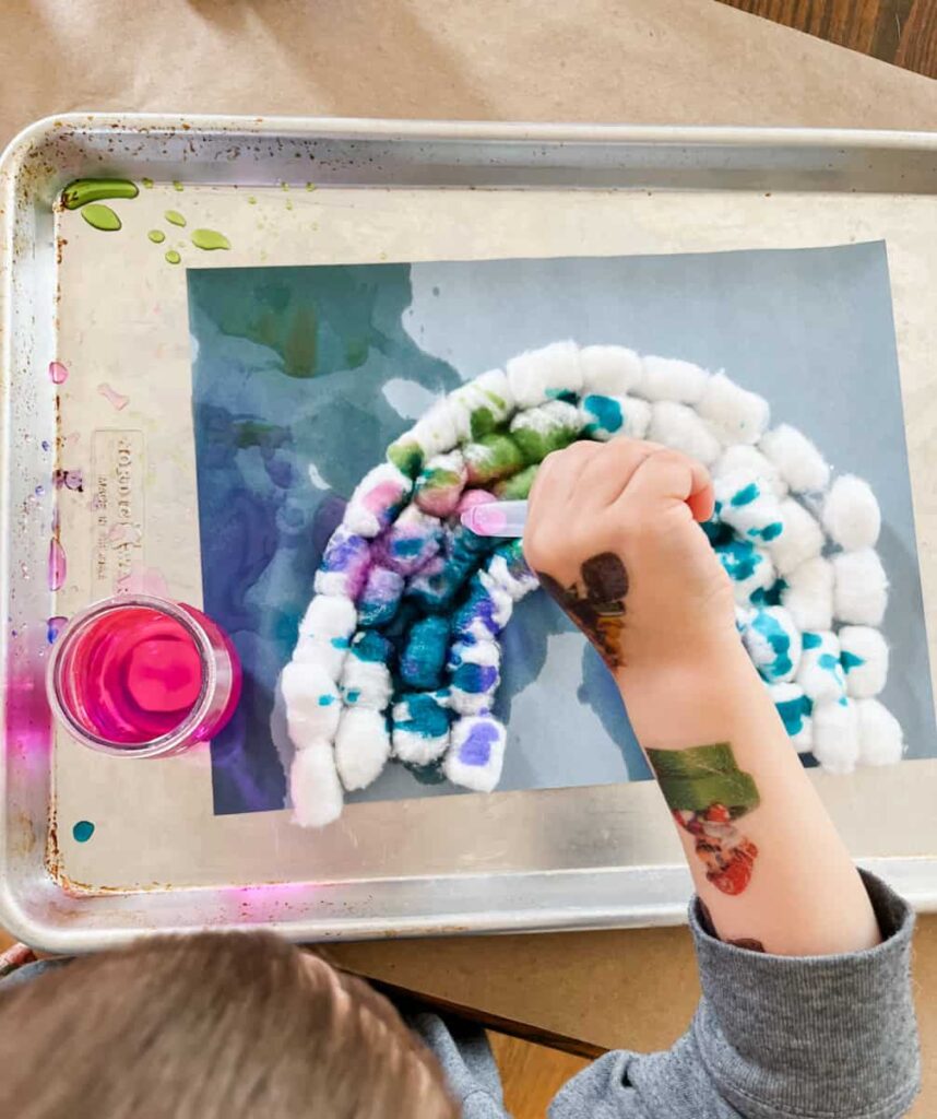 small childs hand using a pipette to drop colors on his rainbow