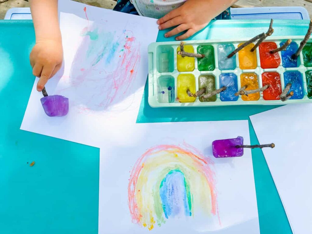 child hand painting with an ice cube on a table next to other ice cube paints.