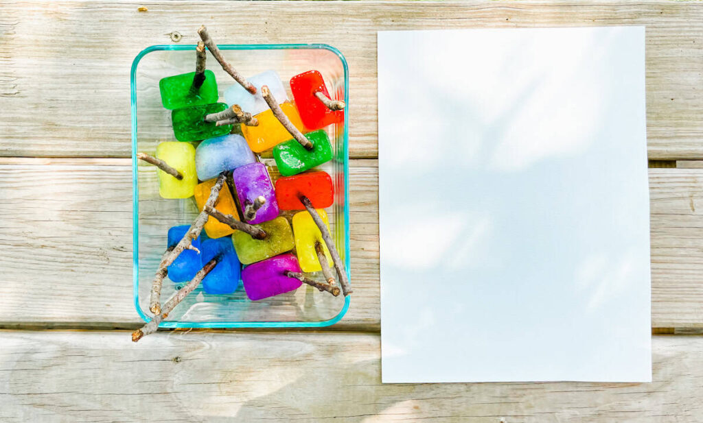 ice cube paint sticks on bench next to a piece of paper