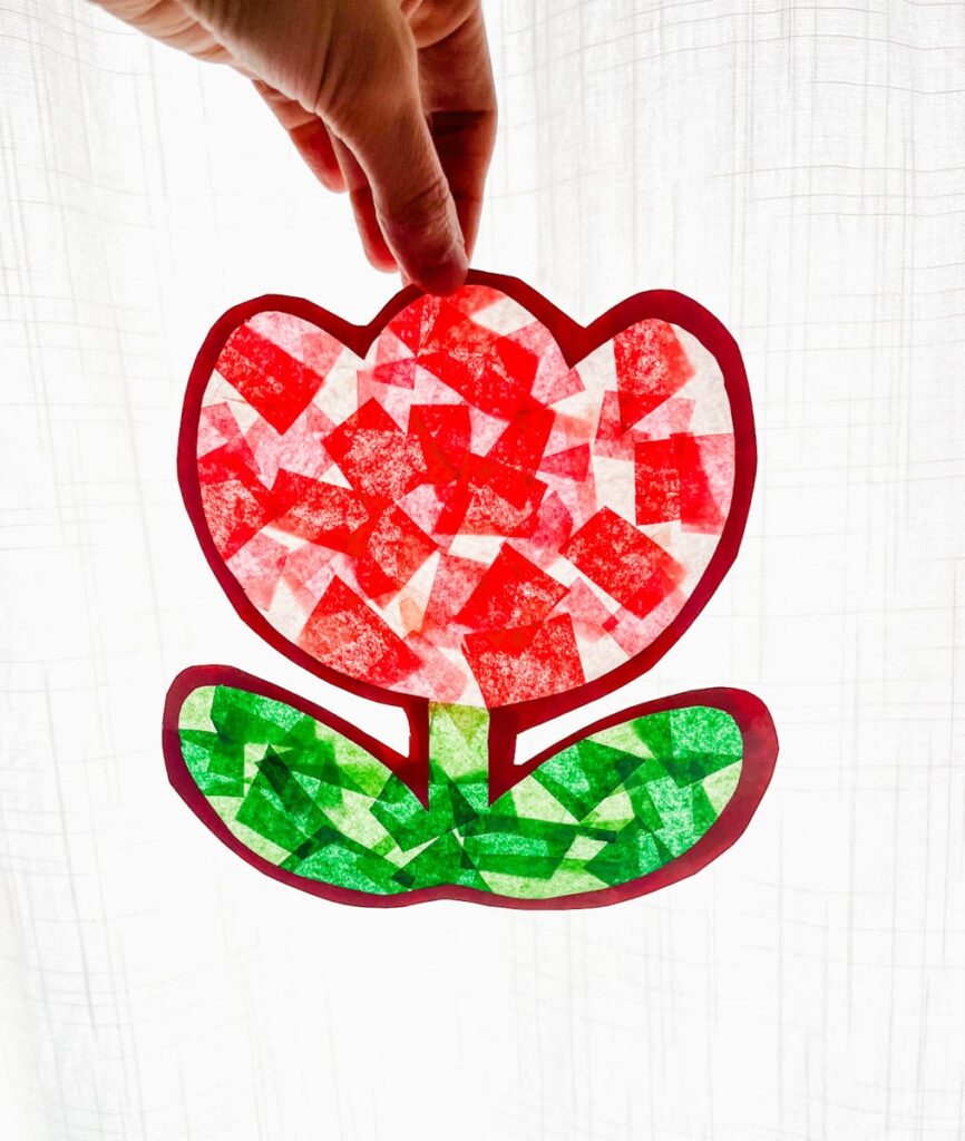 cut out tulip suncatcher being held up in front of a white curtain