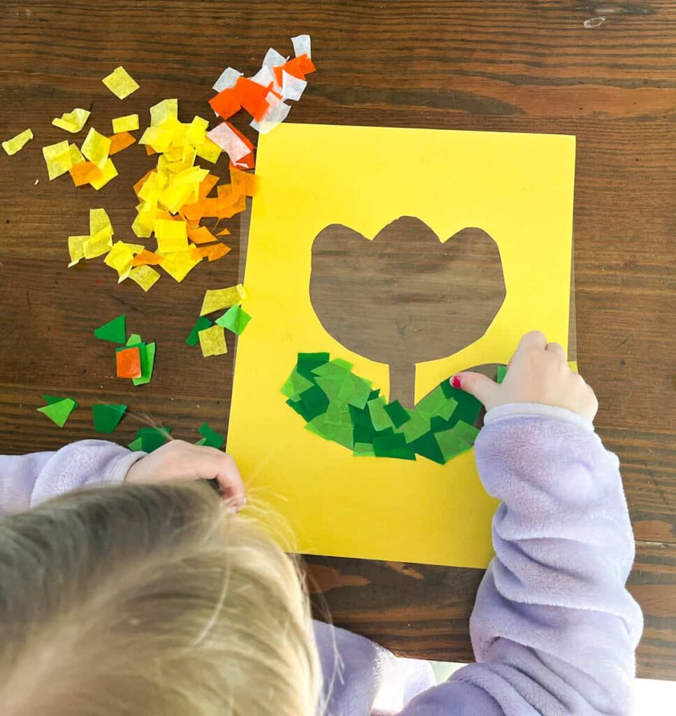 childs hand putting tissue paper on the tulip frame next to cut out pieces of tissue paper