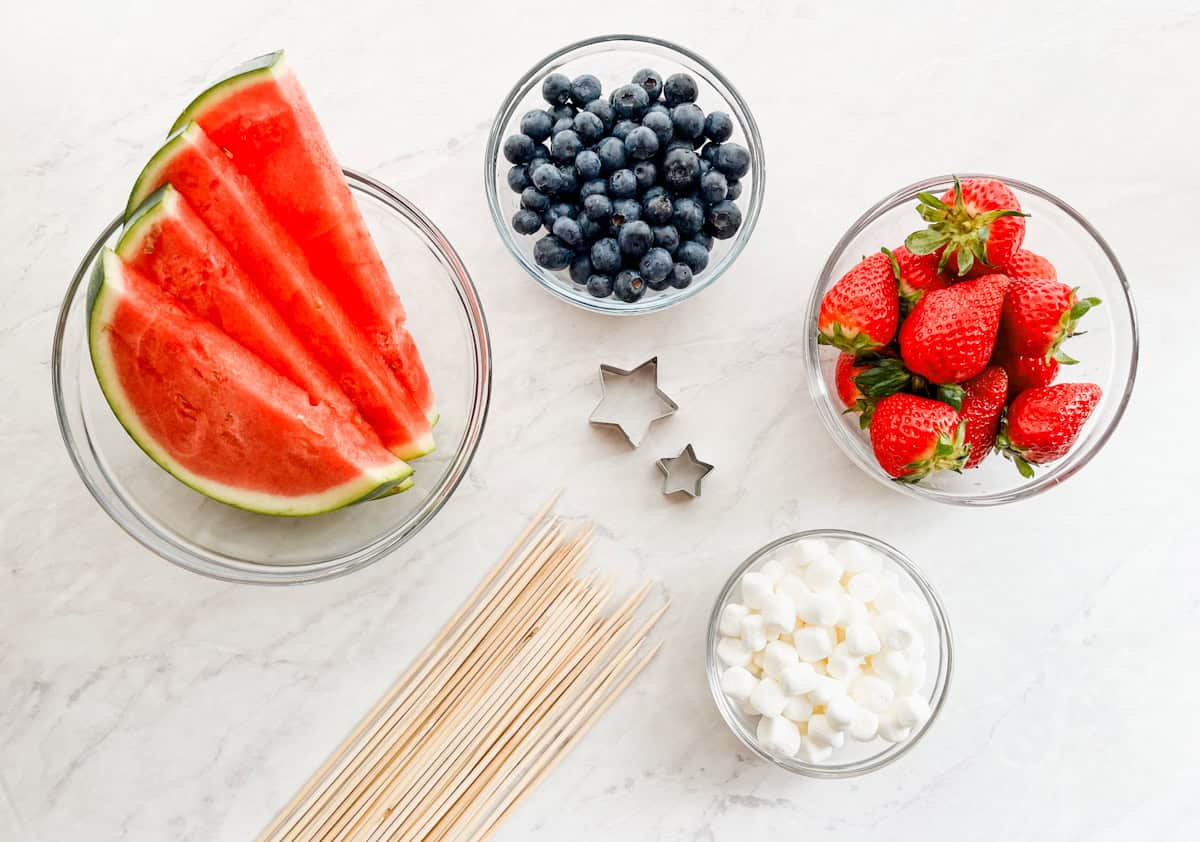 Watermelon, blueberries, strawberries, mini marshmallows, bamboo skewers and small star cookie cutters sitting on the counter.