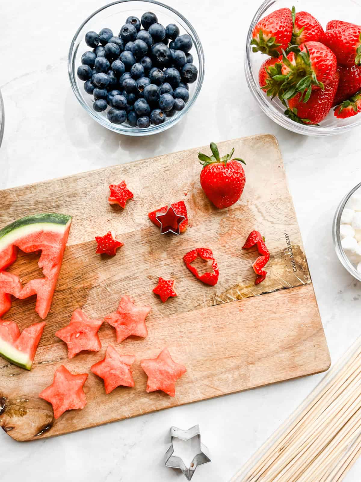 Watermelon and strawberry cut out into star shapes on a cutting board.