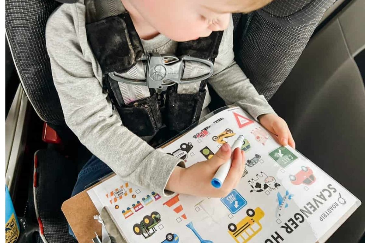 child in car seat working on the road trip scavenger hunt that is laminated on clipboard.