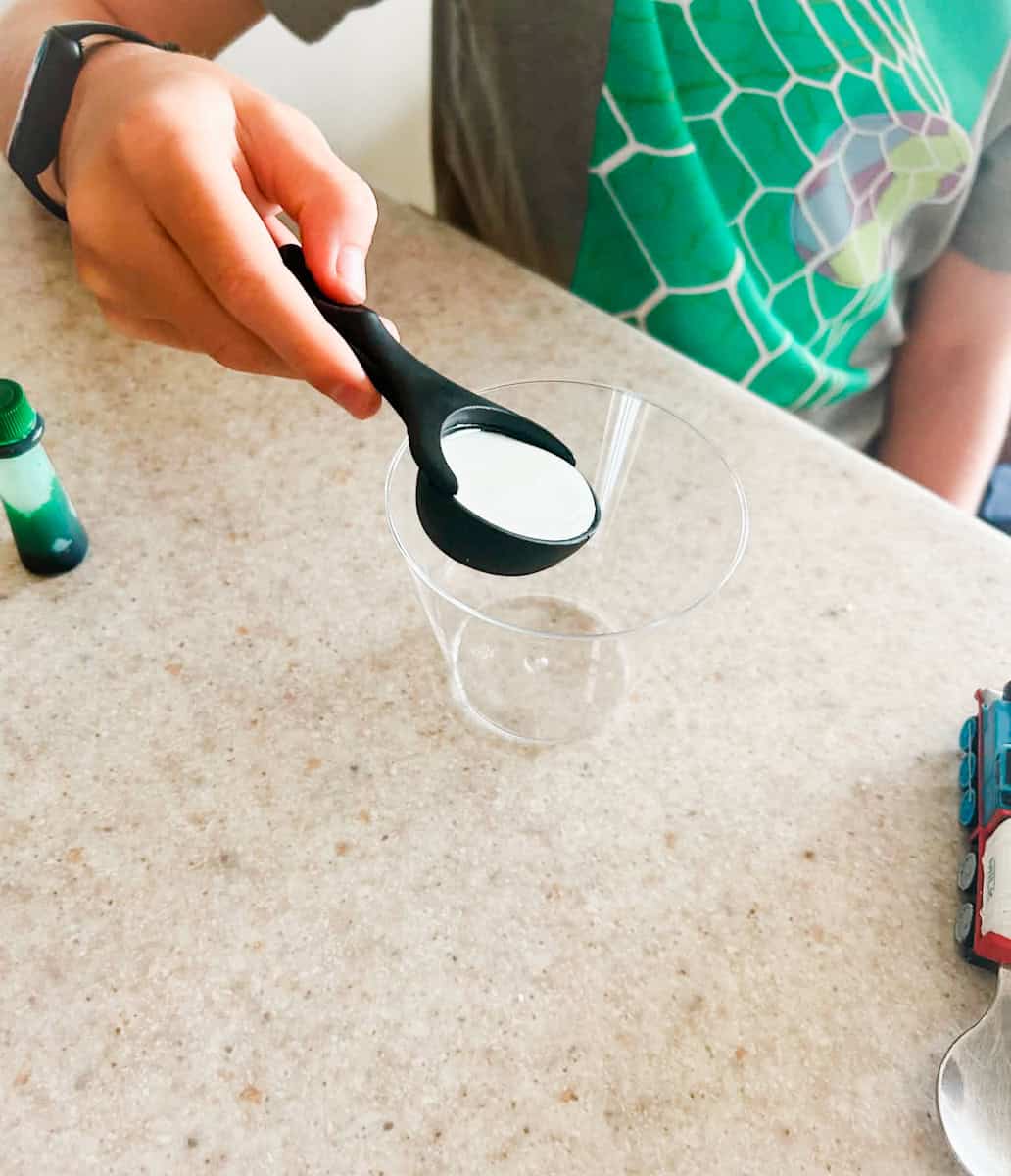 child pouring glue into clear cup.