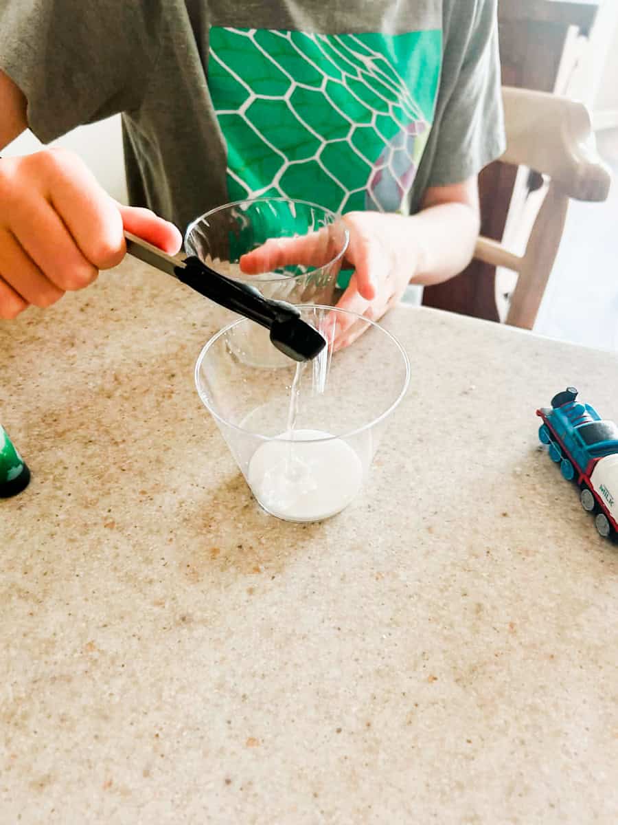child pouring borax solution into cup with glue.
