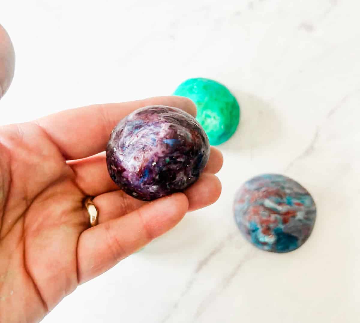hand holding purple bouncy ball with 2 other bouncy balls behind them.