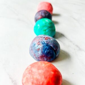 5 bouncy balls all in a line on table, they are all different colors.