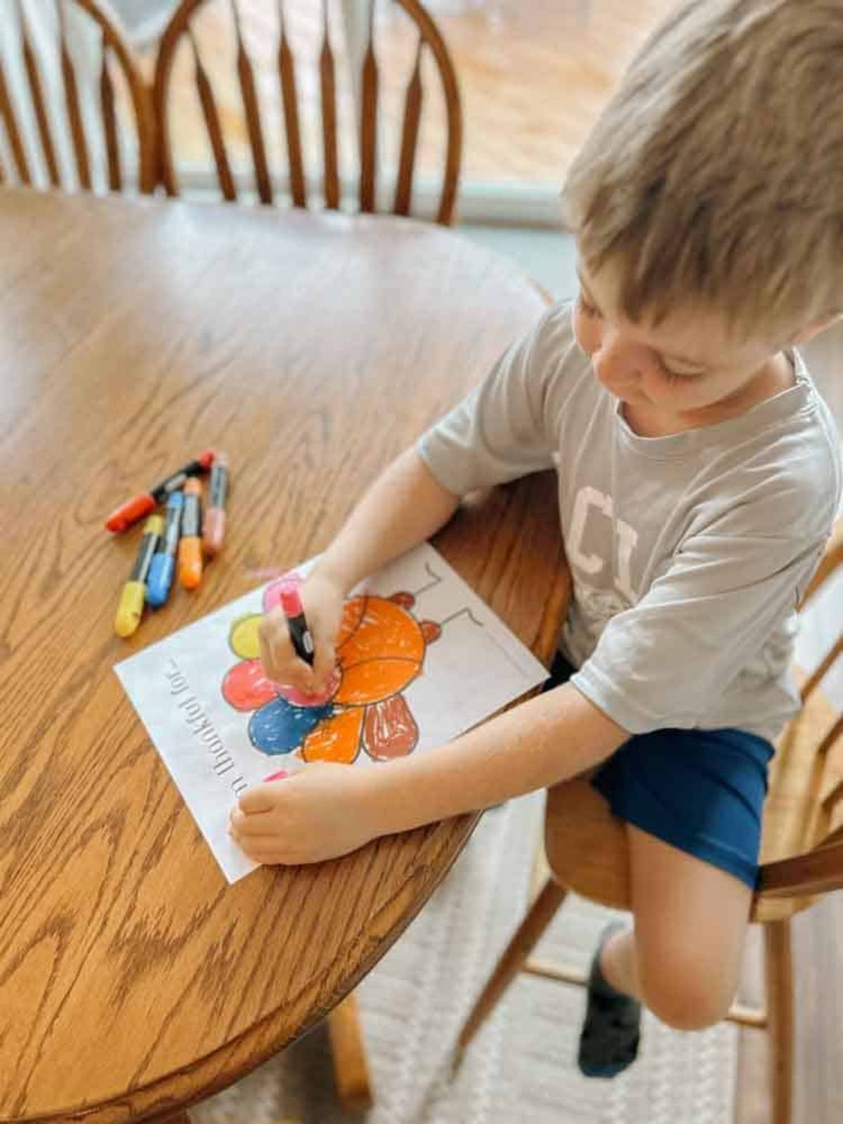 child sitting at table with crayons and the Thanksgiving printable turkey, child is coloring it in.
