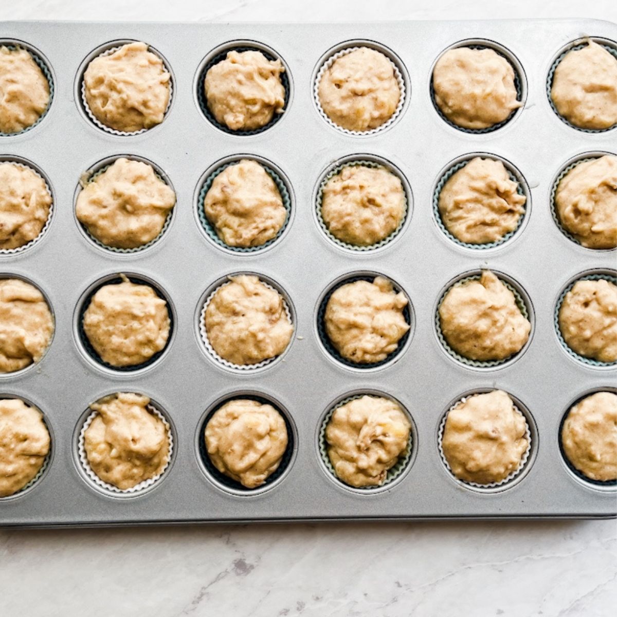 Mini muffin tins filled with muffin batter on the counter.